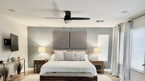 A bedroom with a bed, a ceiling fan, a mounted TV, and a wall with a decorative panel. - Gorgeous Custom Home, Resort Amenities, Heated Pool, Stay in Luxury (Tempe)