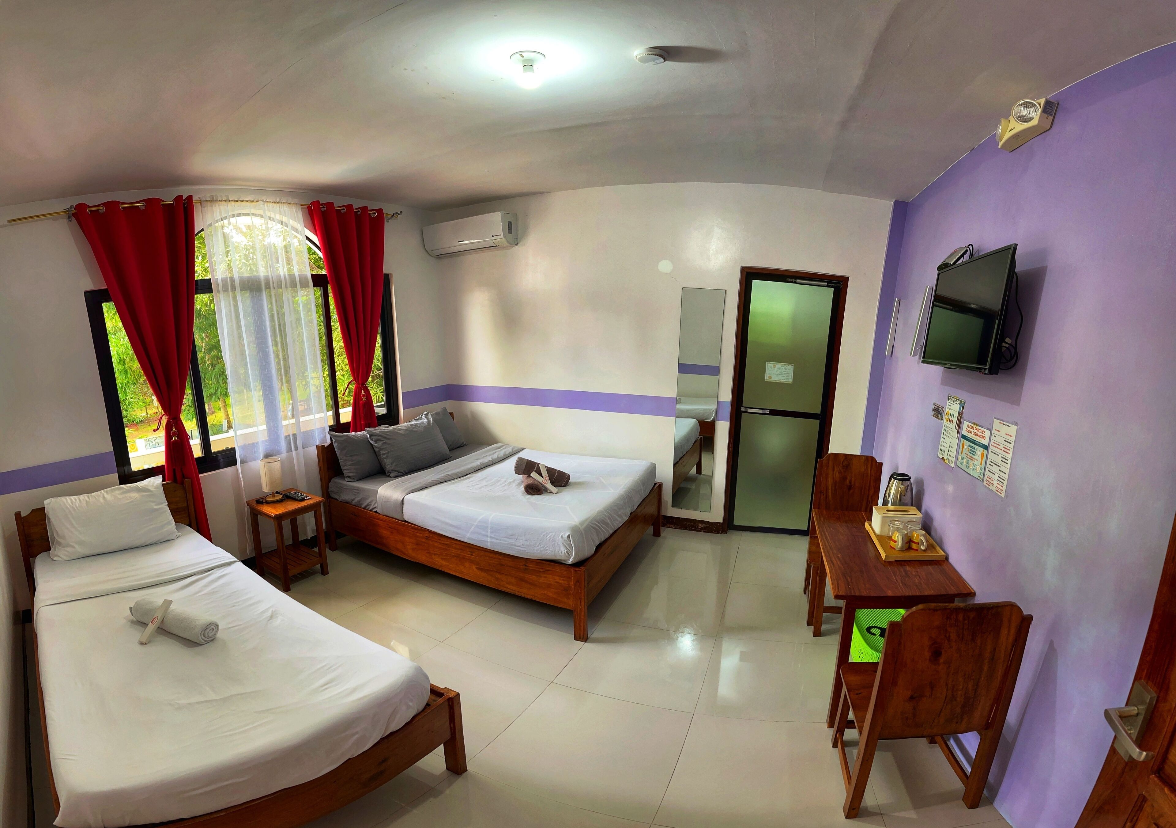A hotel room with two beds, a desk, a TV, and a refrigerator.