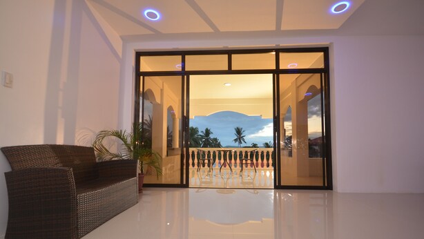 A lobby with a wicker sofa, a glass door leading to a balcony with a view of palm trees and a mountain. - White Summerville Tourist Inn (Busuanga)