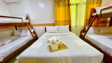 A hotel room with two bunk beds, a central bed, and a window with curtains.