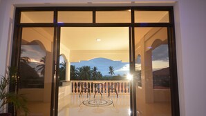 A modern hotel entrance with a glass door reflecting a sunset view, a balcony with chairs, and a decorative floor pattern. - White Summerville Tourist Inn (Busuanga)