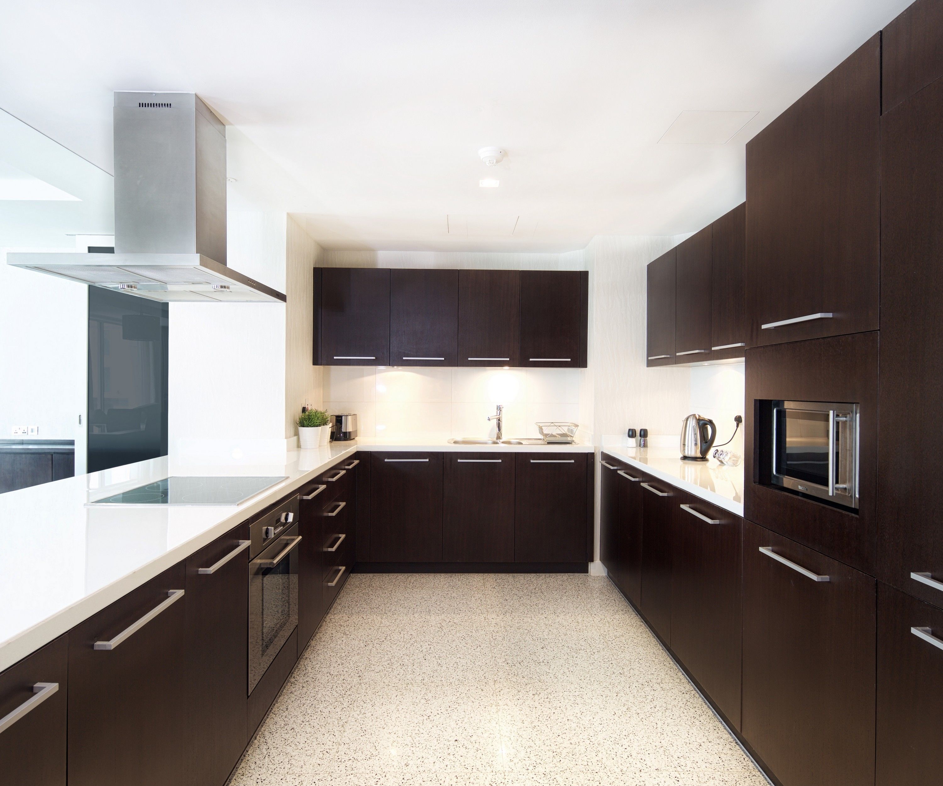 A modern kitchen with dark cabinetry, white countertops, and a speckled floor.