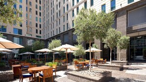 An outdoor patio area with multiple tables and chairs, surrounded by trees and umbrellas.