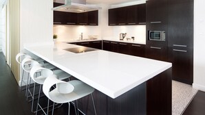 A modern kitchen with dark cabinetry, a white countertop, and bar stools.