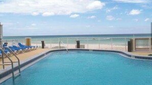 Una piscina con vista al océano, rodeada de sillas de descanso y una valla.