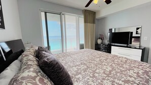Un dormitorio con cama, televisor, cómoda y balcón con vista al océano.