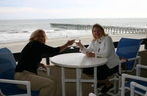 Two people toasting at a round table with a view of the beach and pier in the background. - Serene Oceanfront Getaway Cherry Grove (North Myrtle Beach)3BR (North Myrtle Beach)