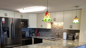 A modern kitchen with granite countertops, stainless steel appliances, and decorative hanging lights. - Serene Oceanfront Getaway Cherry Grove (North Myrtle Beach)3BR (North Myrtle Beach)