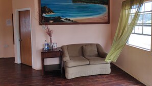 A room with a painting of a beach scene, a sofa, a small table with a vase, and a door labeled '6B'. - Aanola Villas 6B Tranquil Privy Boudoir (Castries)