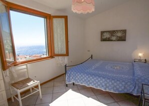 A bedroom with a bed, a chair, a window with a view, and a wall-mounted picture.