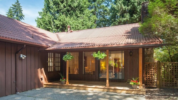 A wooden house with a tiled roof, a porch with potted plants, and a stone pathway leading to the entrance. - Capilano Forest Little House (District of North Vancouver)