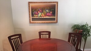 A dining room with a round wooden table, four wooden chairs, a framed painting on the wall, and a potted plant. - Capilano Forest Little House (District of North Vancouver)