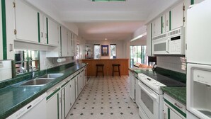 A kitchen with white cabinets, green accents, a central island with stools, a microwave, and a stove. - Capilano Forest Little House (District of North Vancouver)