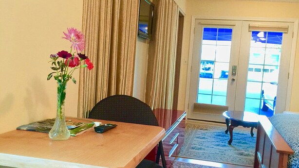Un comedor con una mesa, sillas, un jarrón con flores, un televisor y vistas a través de puertas de cristal.