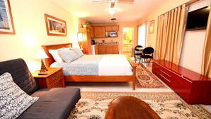 Habitación de hotel con cama, sofá, escritorio, televisor, kitchenette y baño.