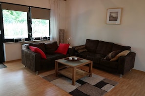 A living room with two sofas, a coffee table, and a window with curtains. - House Deichschaf, Germany (Butjadingen)