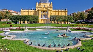 A large yellow building with a fountain in the center surrounded by pigeons. - Apartment in Zagreb with Terrace, Air condition, WIFI, Washing machine (3798-1) (Zagreb)