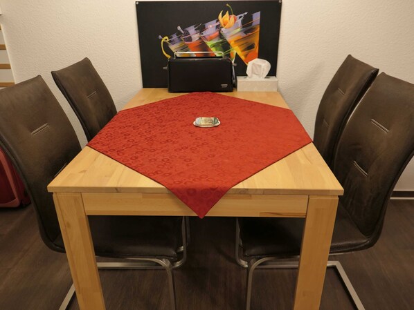 A dining table with a red tablecloth, surrounded by four chairs, and a black toaster on the table.