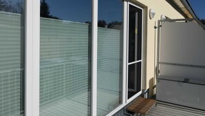 Ein modernes Gebäude mit großen Glasfenstern, einem Metall-Dach und einer Holzterrasse.