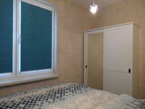 A room with a bed, a window with blinds, a door, and a ceiling light fixture.