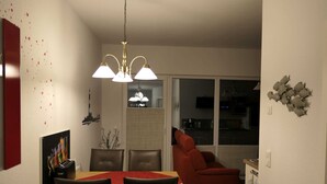 Ein Essbereich mit Tisch und Stühlen, ein rotes Sofa, eine Chandelüster und eine Küche im Hintergrund.