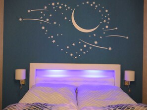A bedroom with a bed, two bedside lamps, and a wall with a starry night design.