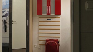Ein Zimmer mit einer Tür, einem roten Koffer, einem an der Wand befestigten Gepäckträger und einem Gemälde.