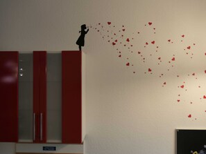 A room with a red and white cabinet, a wall with heart-shaped decorations, and a small silhouette of a person.