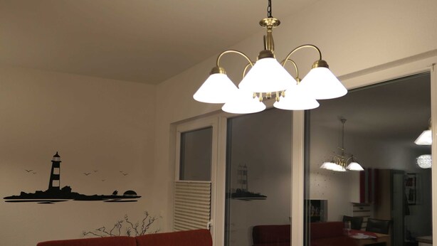 Ein Zimmer mit einem roten Sofa, einer Kristallleuchter, einem Fenster mit Jalousien und einer Wandsticker mit einem Leuchtturm.