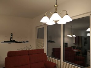 A room with a red sofa, a chandelier, a window with blinds, and a wall decal of a lighthouse.