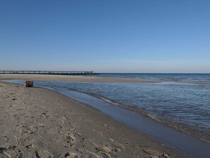 A beach with a pier extending into the water, sandy shore, and footprints in the sand.