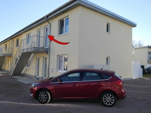A red car parked in front of a building with a staircase leading to a balcony.
