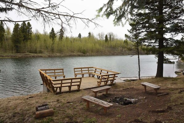 A wooden deck with benches and picnic tables by a lake, surrounded by trees.