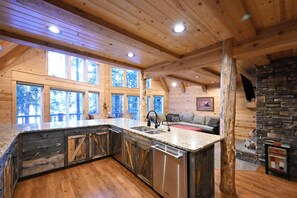 A spacious kitchen with a large island, wooden ceiling beams, and a stone fireplace.