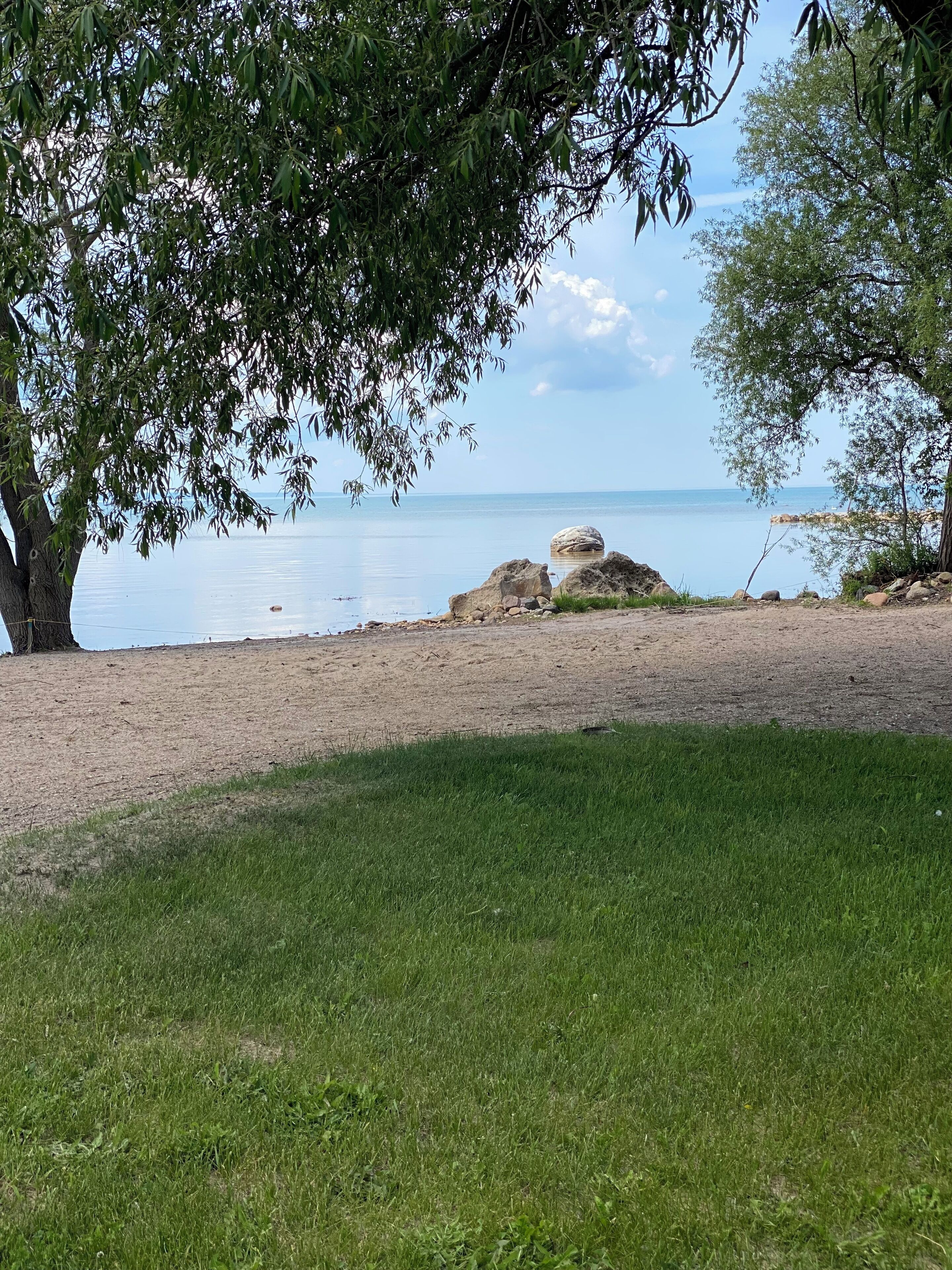 A grassy area with a view of a calm body of water and a rocky outcrop.