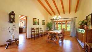 Une cuisine spacieuse avec des poutres en bois, un coin repas doté d’une grande table et une vue sur le jardin par les fenêtres.