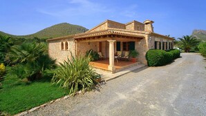 Une maison en pierre dotée d’un patio, entourée de verdure et avec une montagne en toile de fond.