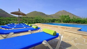 A poolside area with lounge chairs and a thatched umbrella.