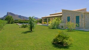 A stone building with a tiled roof, a swimming pool, and a mountain in the background.