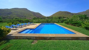Une piscine rectangulaire à l’eau d’un bleu limpide, entourée d’une pelouse bien entretenue et bordée d’une rangée de chaises longues bleues.