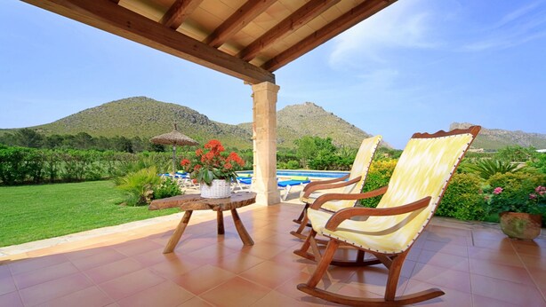 A patio with a wooden table and two rocking chairs overlooking a pool and mountains.