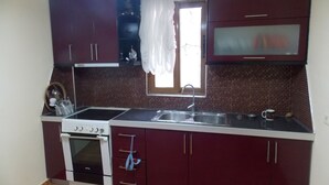 Cocina compacta con armarios oscuros, estufa blanca y pileta doble.