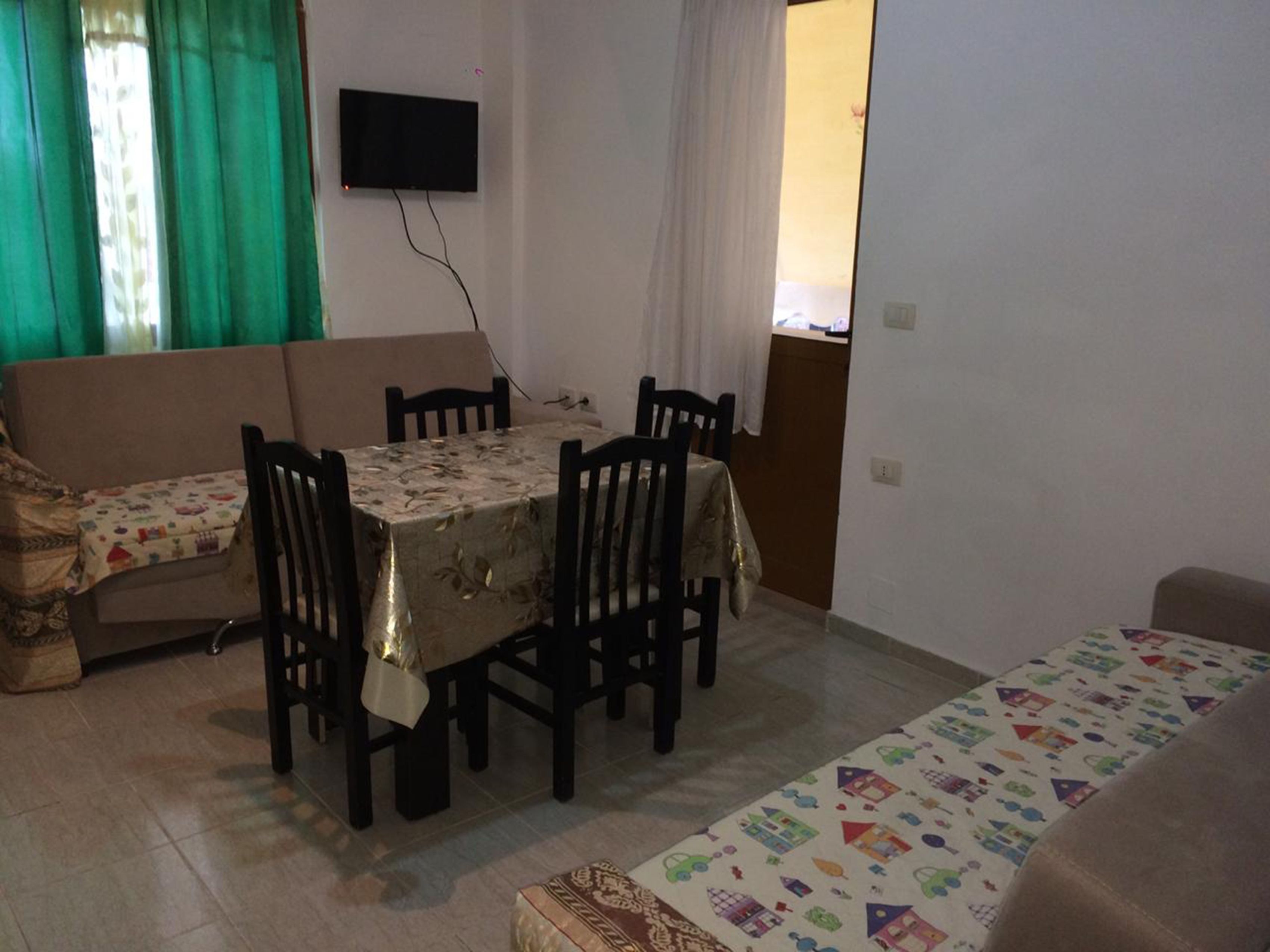 A dining area with a table set for four, surrounded by chairs. A television is mounted on the wall above the table.