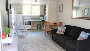 A compact living space with a kitchenette, a dining area, and a seating area with a couch and chairs. - Lakeside apartment with boat ramp & jetties (Koutu)