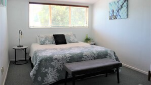 A bedroom with a bed, a bench, a bedside table, a lamp, a window with blinds, and a wall-mounted artwork. - Lakeside apartment with boat ramp & jetties (Koutu)