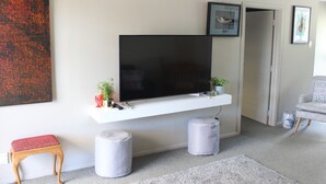 A modern living room with a mounted TV, a small bench, two ottomans, and a grey carpet. - Lakeside apartment with boat ramp & jetties (Koutu)