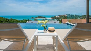 A poolside view with lounge chairs, a table with a hat and flowers, and a scenic ocean and island view.