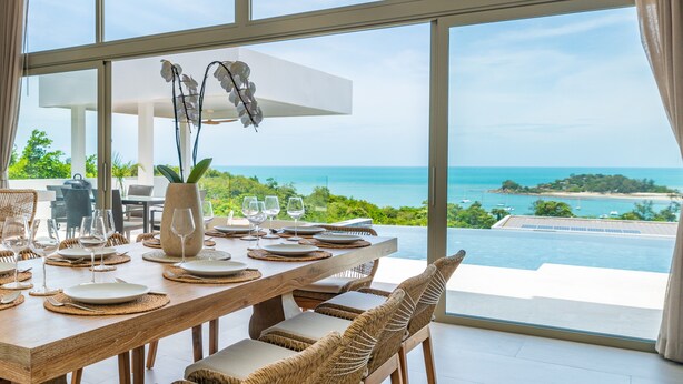 A dining area with a table set for six, overlooking a scenic ocean view.