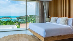 A bedroom with a large bed, a wooden headboard, a view of the ocean, and a ceiling fan.