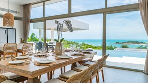 A dining area with a large table set for six, overlooking a scenic ocean view.